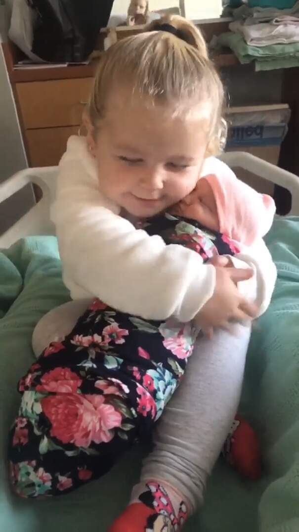 Bambina di 3 anni tiene in braccio la sorellina neonata per la